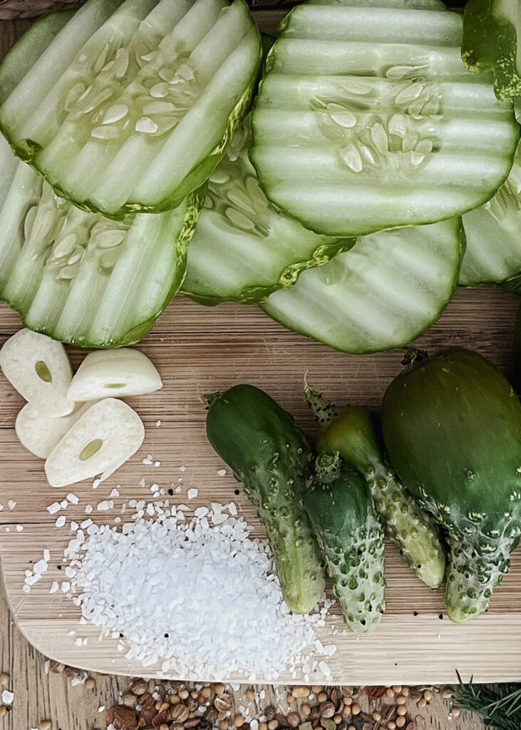 crinkle cut cucumbers, freshly chopped garlic, small gherkins, and spices on wooden cutting board
