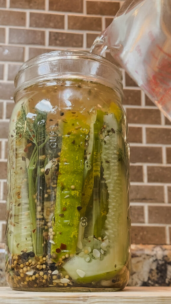 Jar of pickles filled with fresh brine against brown subway tile background