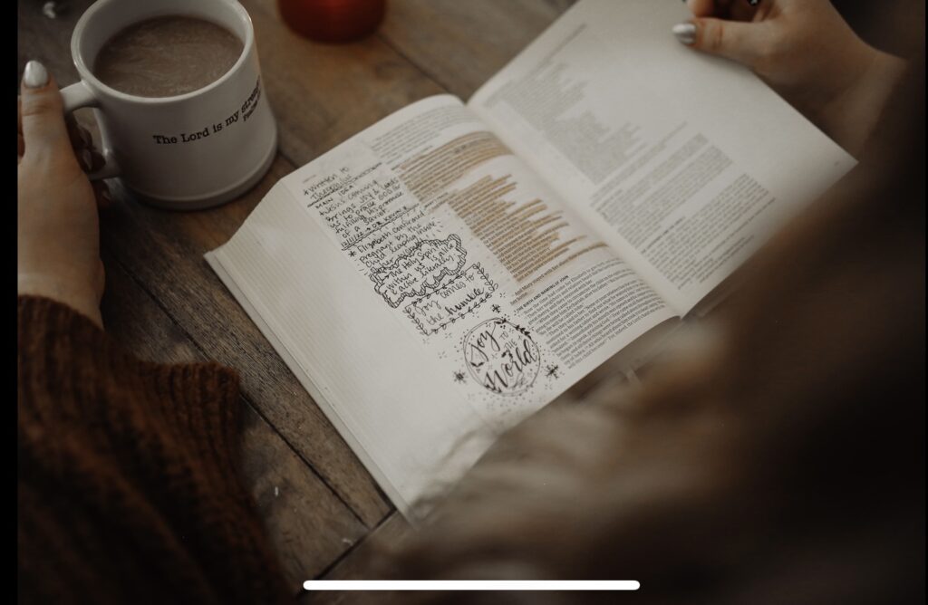 Bible with highlighted text and notes in margin on table next to coffee cup
